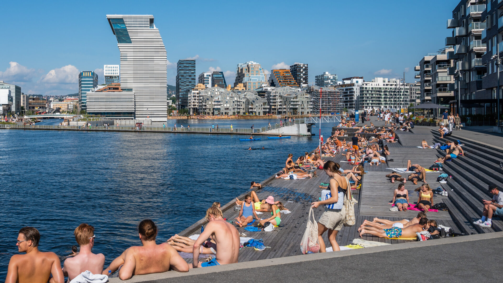 Mennesker som soler seg på brygge med Munchmuseet i bakgrunnen. Foto.