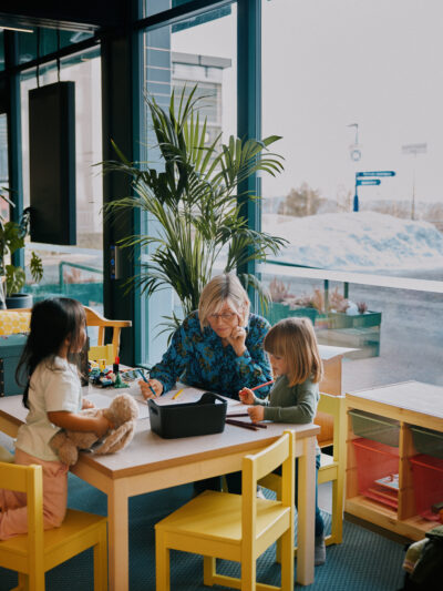 Leksehjelp på Romsås kulturhus. Kvinne og to barn rundt et bord.